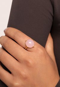 Goldring mit einem großen, glatten rosa Stein. Der Ring ist dünn und elegant, mit einer polierten Oberfläche. Hautstruktur auf der Hand sichtbar.