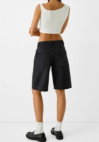 Mustat denimbermudashortsit, joissa on rento istuvuus, kahdella takataskulla ja kiristettävällä vyötäröskannalla. Yhdistettynä valkoisiin nilkkasukkiin ja mustiin kenkiin.