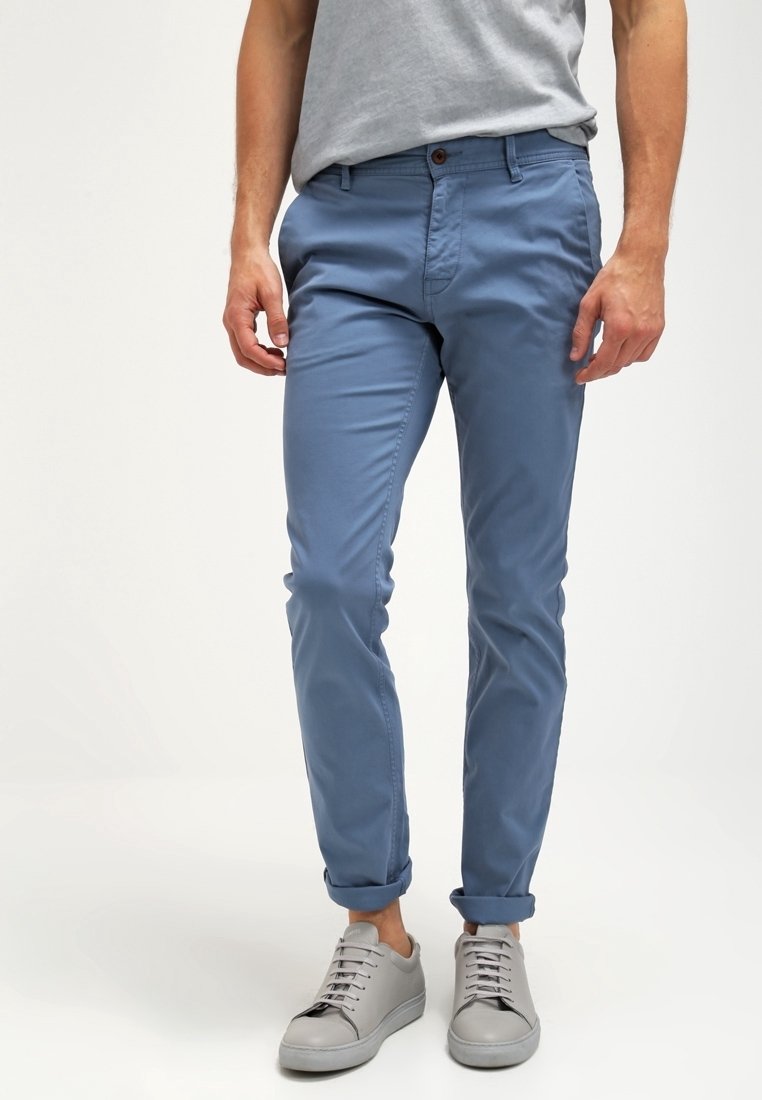 Ljusblå, slim-fit chinos med en jämn textur, som har en brun knappstängning och uppvikta ärmslut, i kombination med ljusgrå sneakers.