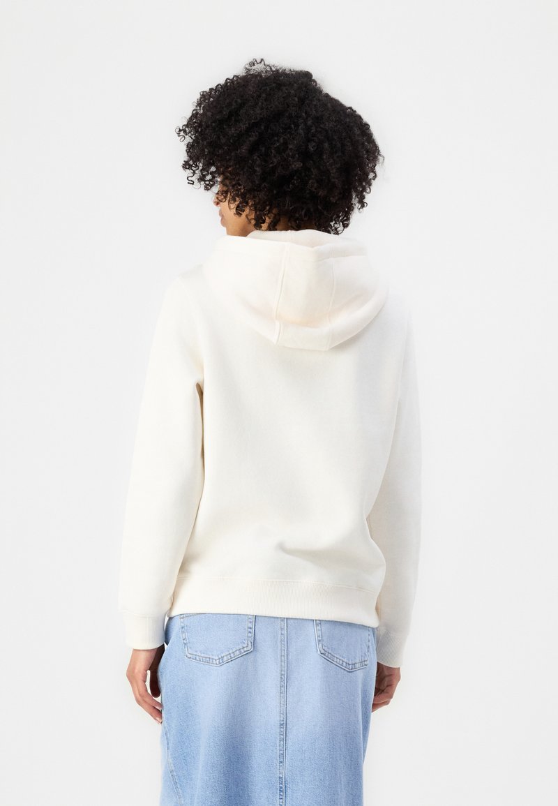 Cremefarbener Hoodie mit weicher Textur und Kapuze mit Kordelzug, kombiniert mit einem hellen Jeansrock mit zwei Gesäßtaschen und einer Naht in der Mitte.