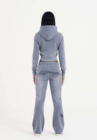 Lichtgrijze hoodie en bijpassende omvlammende broek met Ed Hardy-logo en grafische accenten; zachte stof met een ontspannen pasvorm en capuchondetail.