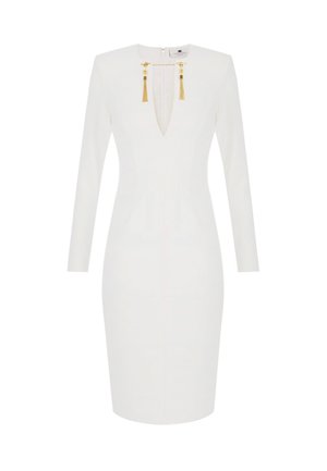 Vestido ajustado de manga larga blanco con escote en V profundo, adornos de cadena dorada y borlas en el cuello, con un dobladillo hasta la rodilla.