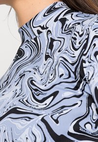 Haut à manches longues avec un col montant. Présente un motif marbré abstrait bleu et noir sur un tissu côtelé, mettant en valeur la texture et le design.