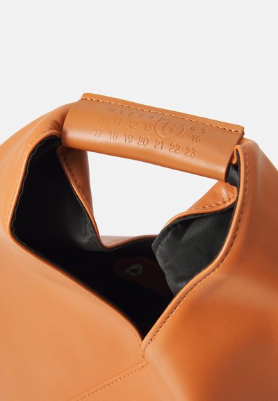 Orange läderväska med rundad topp. Interiör fodrad med svart tyg. Handtaget har präglade siffror längs kanten.