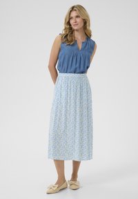 Top din denim albastru deschis, fără mâneci, cu un decolteu cu tăietură, asortat cu o fustă midi cu model floral în nuanțe de albastru și galben, și pantofi plata bej.