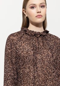 Leopardenmuster-Bluse aus durchsichtigem Stoff mit rüschiertem Ausschnitt, in Brauntönen und Schwarz; langärmlig mit lockerer Passform.