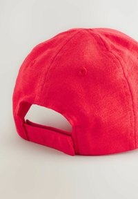 Gorra de béisbol de tela roja con corona redondeada, correa ajustable en la parte posterior y textura suave. Presenta ojales de ventilación.