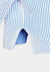 Stickad plagg med växlande blå och vita vertikala ränder. Tyget har en ribbad textur med en diskret utskärning vid nederkanten.