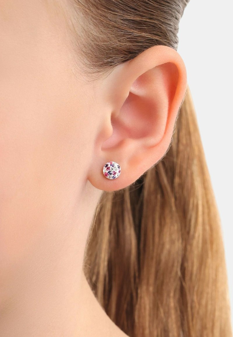 Pendientes de aro con un patrón floral multicolor sobre un fondo blanco, situados contra un primer plano de una oreja y cabello.