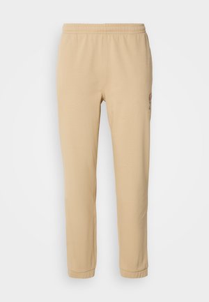 Beige bomullssweatpants med elastiskt midjeband, avsmalnande ben och sidobroderi, som har en mjuk textur och en enkel design.