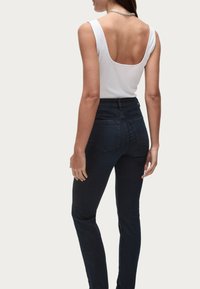 Vit ärmlös topp med rundad rygg, i kombination med mörkblå högmidjade jeans. Jeanssen har bakfickor och en åtsittande design.