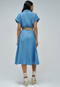Svetlo modra džinsasta obleka s kratkimi zavihanimi rokavi, pasom v pasu in brezskrbno A-linijo, dopolnjena z natikači na klin.