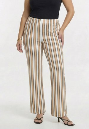 Femme portant un pantalon beige taille haute à rayures verticales blanches et noires, un haut noir sans manches et des sandales noires à talons.