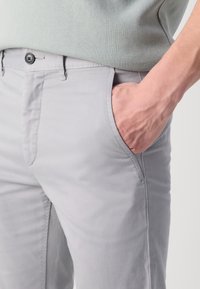 Light gray cotton pants with a smooth texture, featuring side pockets and a button closure. A close-up view shows detailed stitching.