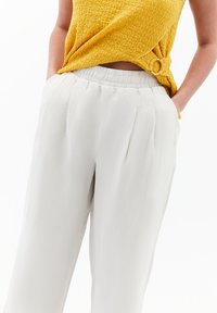 Lätta, krämfärgade byxor med elastisk midja, subtila veck och sidofickor, i kombination med en strukturerad gul topp.