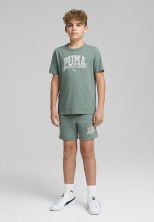 Zelena bombažna majica s grafiko "PUMA sports club", v kombinaciji s ujemajočimi se kratkimi hlačami. Ima bele poudarke in klasične bele superge.