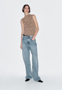 Tan sleeveless top paired with light blue wide-leg jeans. The outfit features a black belt and pointed black shoes. Simple background.