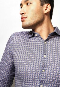 Langärmliges Hemd in Blau mit einem geometrischen Muster in Orange und Creme, aus leichtem Stoff gefertigt, mit einem spitzen Kragen und Perlmuttknöpfen.