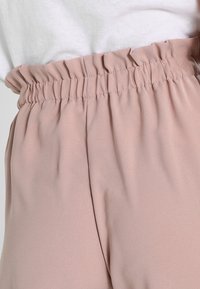 Vaaleanpunaiset, joustavavyötäröiset housut, valmistettu pehmeästä, kevyestä kankaasta; vyötäröllä rypytetty rakenne mukavan istuvuuden takaamiseksi.