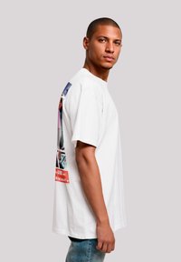 Weißes Baumwoll-T-Shirt mit kurzen Ärmeln, mit grafischen Drucken auf der Rückseite in blauen, rosa und roten Tönen. Lässige Passform, schlichtes Design.