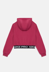 Skraćeni ružičasti dukserica s crnim elastičnim pojasom na kojem je natpis "NIKE PRO." Ima kapuljaču i duge rukave. Glatka tekstura tkanine.