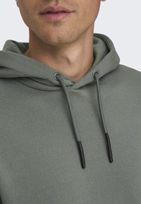 Sweat à capuche gris en polaire avec cordons de serrage munis d'embouts en plastique noir, un col rond et une texture douce et lisse.