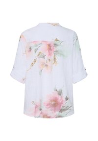 Blouse blanche à manches retroussées avec de grands motifs floraux roses et verts dans le dos.