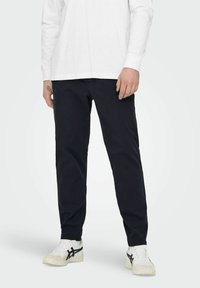 Navyblauwe chinos gemaakt van katoen, slim fit met zijzakken, gedragen met een wit overhemd met lange mouwen en witte sneakers.