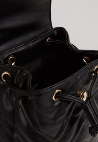 Schwarze Lederhandtasche mit einem geqilteten Chevron-Muster, goldenen Beschlägen, Kordelzugverschluss und einem geräumigen Innenraum.