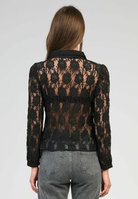 Veste en dentelle noire avec motifs floraux, col à revers, manches longues, dos transparent et ourlet uni.