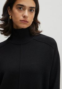 Schwarzer Rollkragenpullover aus strukturiertem Strickstoff, mit einem gerippten Ausschnitt und dezenten Schulter Nähten. Sauberes und minimalistisches Design.