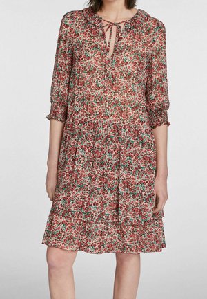 Robe fleurie avec un petit col, un décolleté en forme de trou de serrure, et des manches trois-quarts avec des poignets à volants. Motif de fleurs rouges et vertes sur un fond clair.