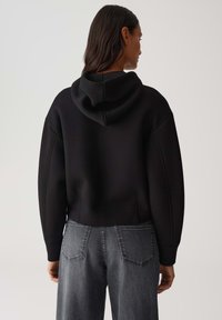 Felpa nera corta con cappuccio e maniche lunghe, abbinata a jeans in denim grigi. Texture liscia, design minimalista, senza hardware o motivi visibili.