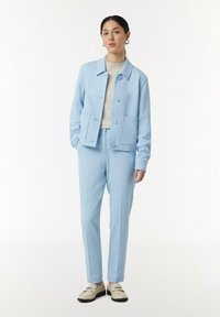 Jasnoniebieska marynarka z dwoma przednimi kieszeniami, zestawiona z dopasowanymi spodniami. Stylizacja zawiera fakturowany beżowy sweter i kremowe mokasyny.