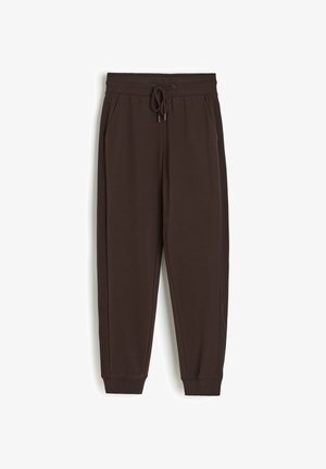 Brązowe zwężane spodnie dresowe z elastycznym pasem, sznurkiem, bocznymi kieszeniami i prążkowanymi ściągaczami, położone płasko na białym tle.