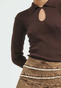 Brown ribbed knit top with a collar and keyhole neckline detail, paired with a brown fringed skirt featuring a patterned waistband.