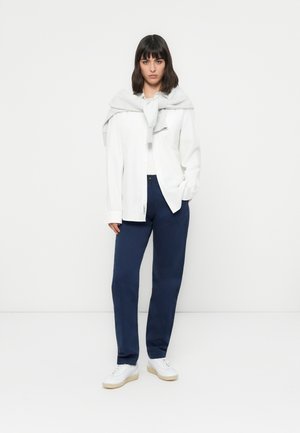 Hvit skjorte, marineblå bukser, lys grå genser knyttet rundt skuldrene, og hvite joggesko. Enkel design, avslappet passform og minimalistisk utseende.