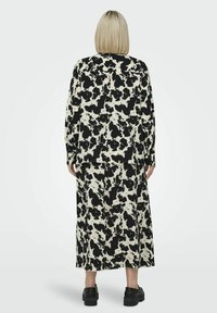 Sæt bestående af bluse og nederdel i sort-hvidt abstrakt print, med løs pasform og lange ærmer, lavet af et glat stof. Sorte sko.