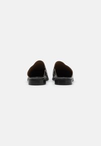 Černé kožené slip-on boty s kulatou zadní částí, plochou podrážkou a hladkým povrchem, s minimalistickým designem a bez viditelných zapínání.