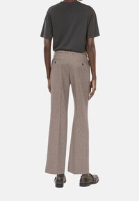 Brązowe spodnie w kratę z szerokimi nogawkami, z tylnymi kieszeniami i gładką fakturą materiału, uzupełnione gładką czarną koszulką.