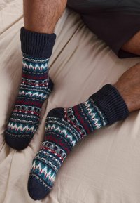 Calze lavorate a maglia con un polsino blu scuro e intricati motivi multicolori in rosso, bianco e verde acqua, su uno sfondo beige.