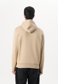Felpa beige realizzata in morbido tessuto, con un ampio cappuccio e polsini a coste. Il design presenta una vestibilità rilassata e uno stile minimalista.