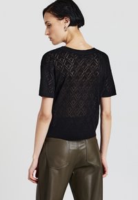 Maglione nero a maglia con motivo a diamante, maniche corte e orlo a costine. Indossato con pantaloni in pelle verde oliva.