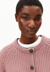 Knitted cardigan in soft light purple with a round collar, button closure, and subtle ribbed texture. Worn over a white shirt.