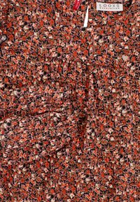 Rood stoffen met een bloemenpatroon en een gerimpelde textuur, met tinten van oranje, roze en zwart. Hangtag toont de merknaam "LOOXS."