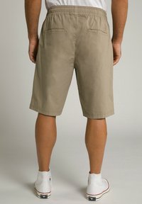 Shorts en kaki avec une coupe décontractée, une taille élastique et deux poches arrière. Portés avec des baskets montantes blanches.