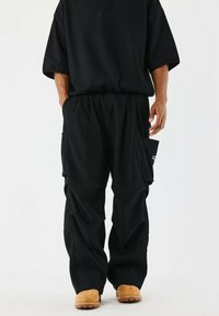 Top oversize nero e pantaloni larghi. Caratteristiche notevoli includono tasche cargo sui pantaloni e calzature di colore chiaro. Tessuto testurizzato.