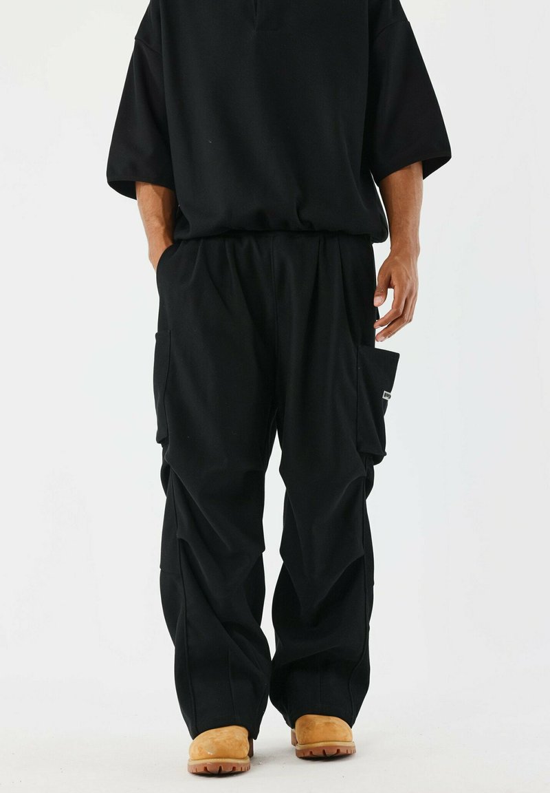 Top oversize nero e pantaloni larghi. Caratteristiche notevoli includono tasche cargo sui pantaloni e calzature di colore chiaro. Tessuto testurizzato.