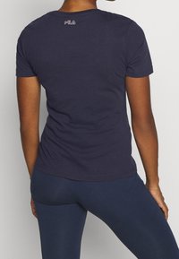 Námořnická modrá tričko vyrobené z bavlny, s přiléhavým střihem a krátkými rukávy, a s malým logem blízko výstřihu na zadní straně.