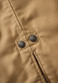 Tissu beige avec doubles boutons-pression noirs fixés par une couture renforcée sur une couture verticale.